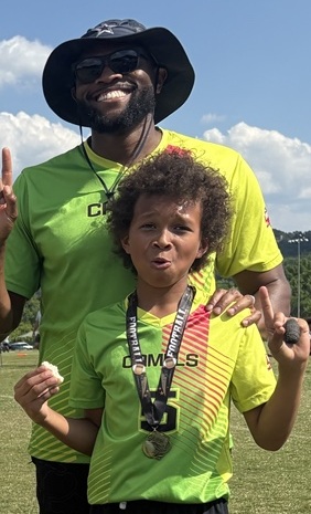 Prentice in his bucket hat with his son on the Camels sidelines